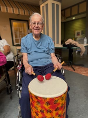 An elderly man playing a drum in an activity room