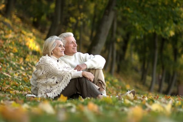 Elderly couple sitting on the grass surrounded by autumn leaves