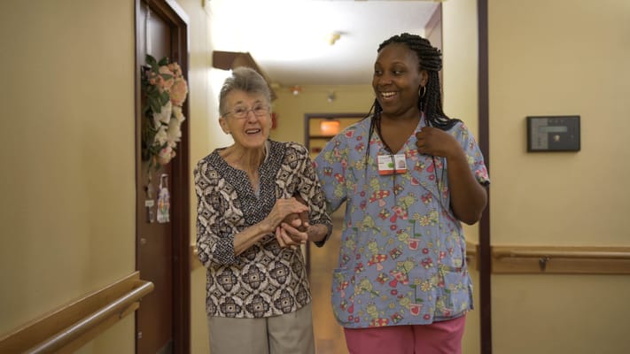 Resident and staff member smiling in a hallway