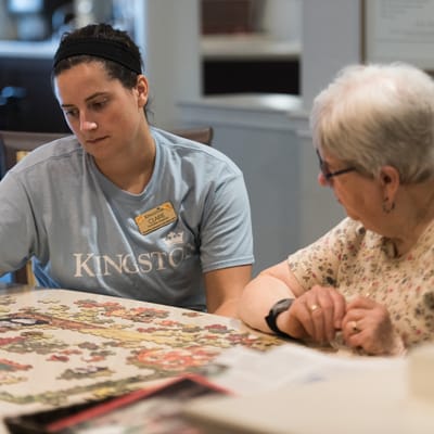Staff assisting a resident with a puzzle at a dining table