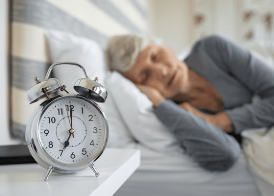 An elderly woman peacefully sleeping in bed with an alarm clock in view