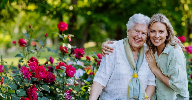 Senior resident and staff member smiling in a rose garden