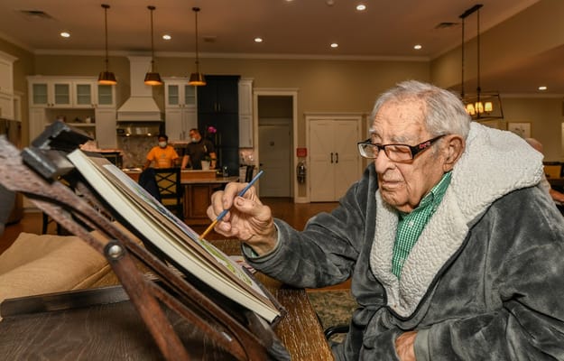 An elderly man painting in a cozy activity room
