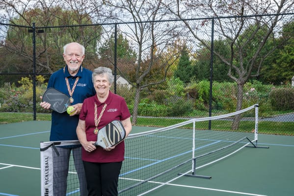 Two residents posing with pickleball paddles on a court