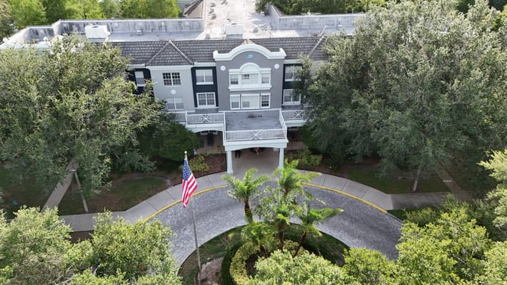 Aerial view of Tampa Gardens Senior Living entrance with palm trees and American flag.