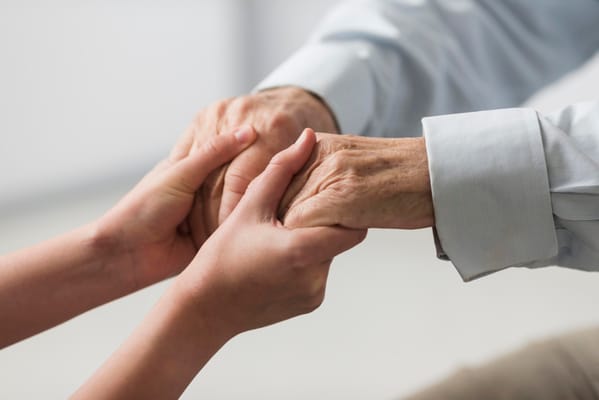 Hands of a caregiver and senior holding each other