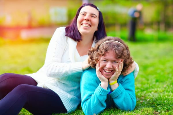Two women smiling while sitting on grass in a garden