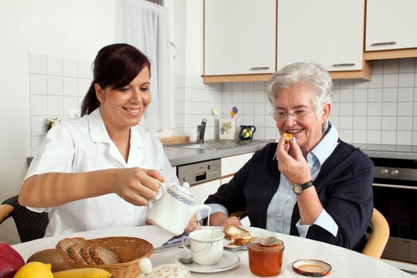 Staff serving food to a smiling resident at a kitchen table