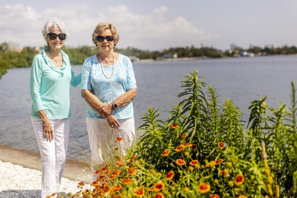Two residents smiling in a garden by the water