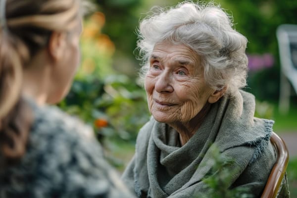 An elderly woman talking with a caregiver outdoors in a garden