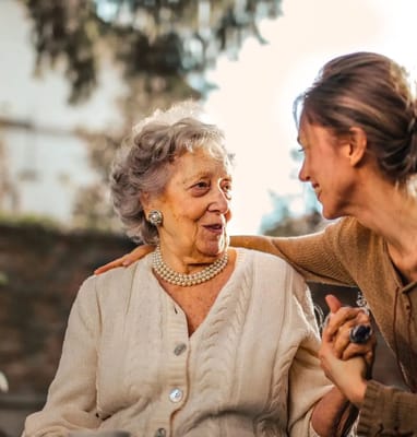 A smiling elderly woman interacting with a caregiver outdoors