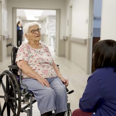 Resident in a wheelchair talking to staff member in a hallway