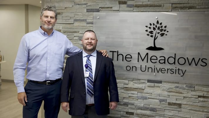 Two staff members posing in front of a facility sign
