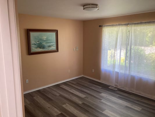 A well-lit private room with a window and wooden flooring