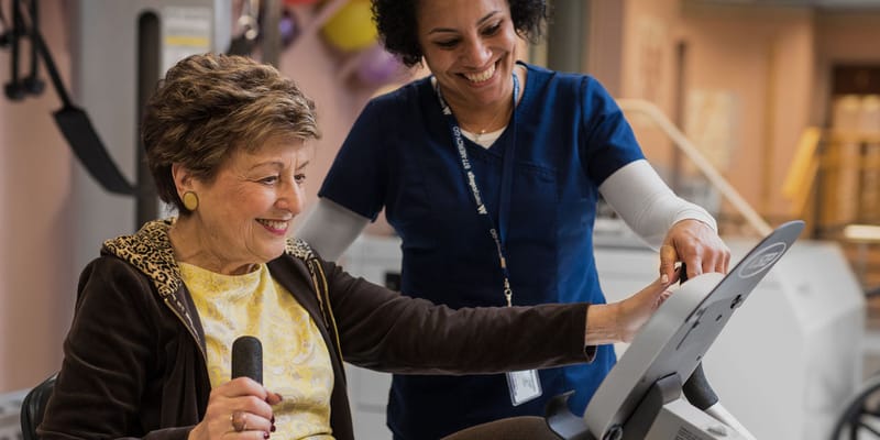 A staff member assisting a resident on exercise equipment