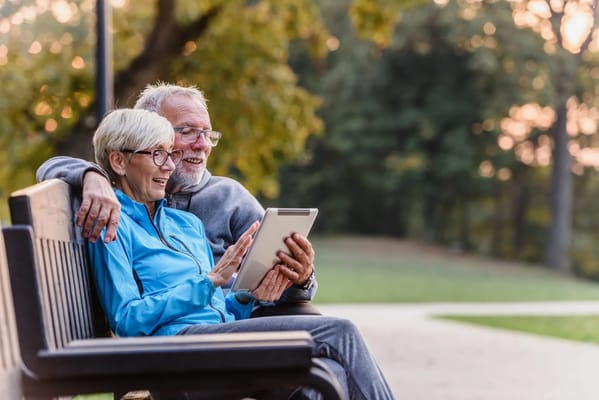 Two seniors enjoying a tablet on a park bench