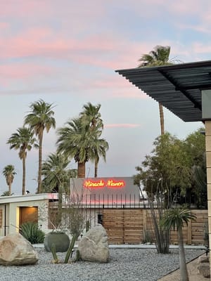 Exterior view of Miracle Manor with palm trees and sunset sky