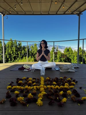 A woman meditating outdoors surrounded by flower petals