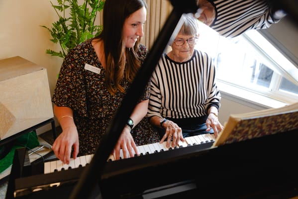 A staff member and a resident playing piano together