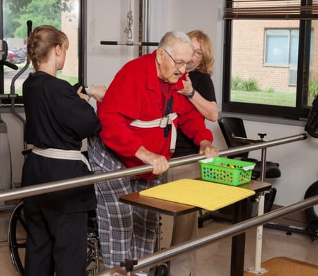 A senior man undergoing physical therapy with staff assistance