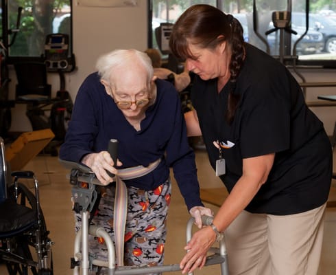 Staff assisting a resident with a walker in a therapy room