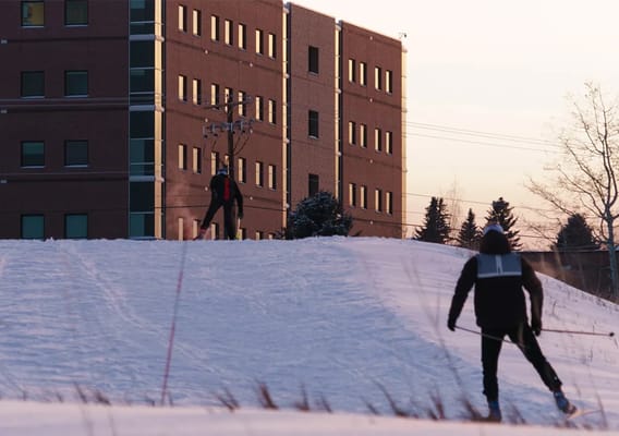 Two individuals skiing on a snowy slope near a building