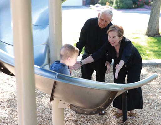 An elderly couple playing with a child at a playground