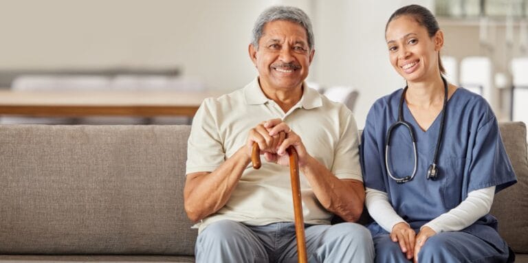 A senior man and a caregiver smiling on a couch