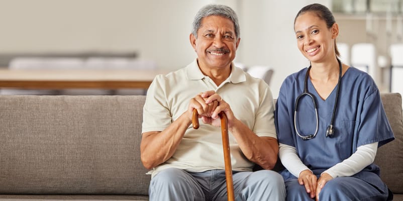 A senior man and a caregiver smiling on a couch