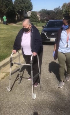Resident using a walker outdoors with staff assistance
