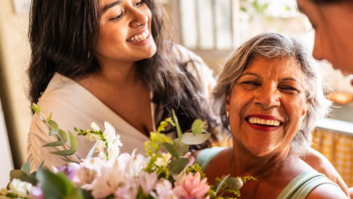 Resident smiling with staff while holding flowers