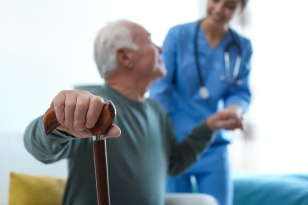 A senior resident with a cane and a nurse in a care setting
