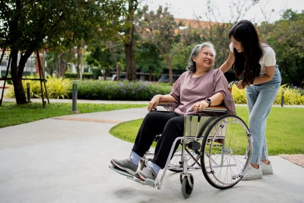 A woman in a wheelchair enjoying time outdoors with a caregiver.