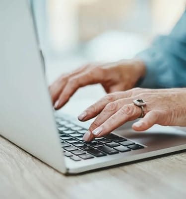 An elderly person's hands typing on a laptop