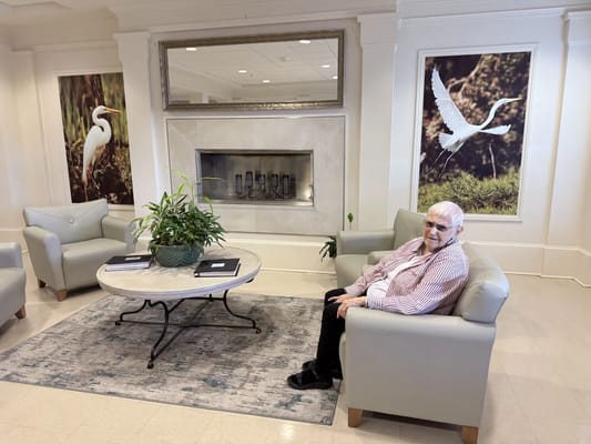 A resident sitting in a common area with plants and artwork