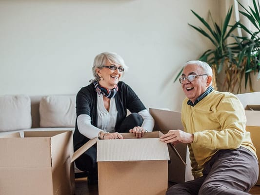 Two seniors joyfully unpacking boxes indoors