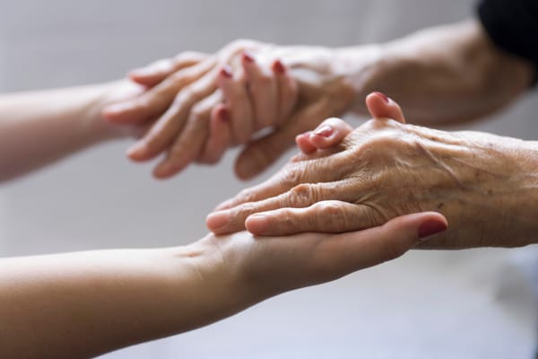 Hands of a caregiver and a senior resident holding each other