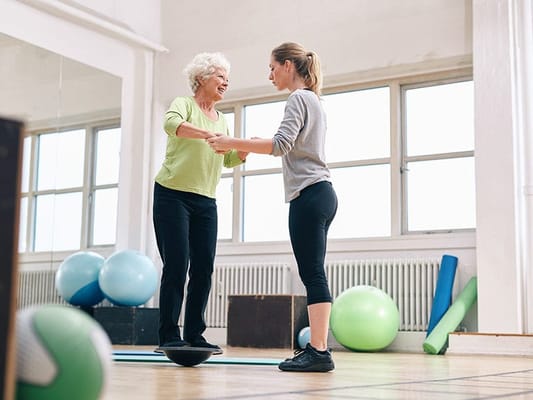 Elderly woman exercising with a staff member in a fitness area