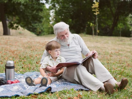 Elderly man reading with a young boy in a park