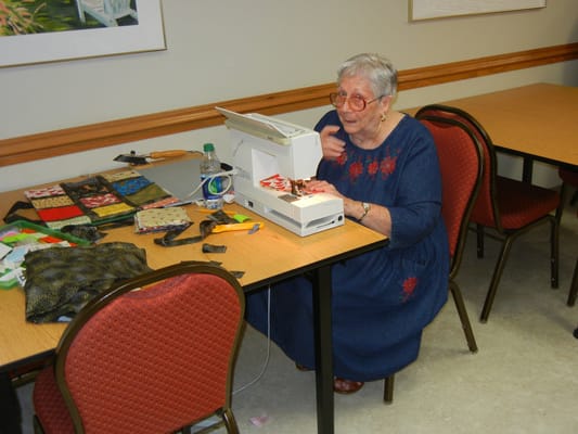 An elderly woman sewing in a craft activity room