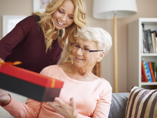 A caregiver helping a smiling resident with a gift