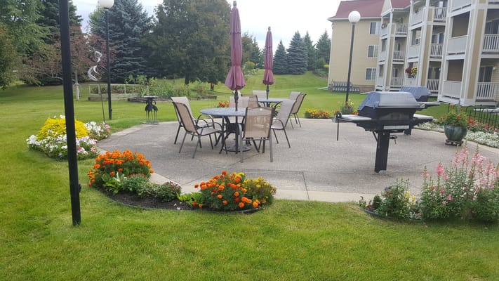 Outdoor patio area with seating and grill surrounded by flowers