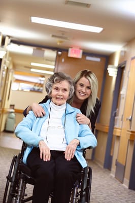 A caregiver assisting a smiling resident in a hallway