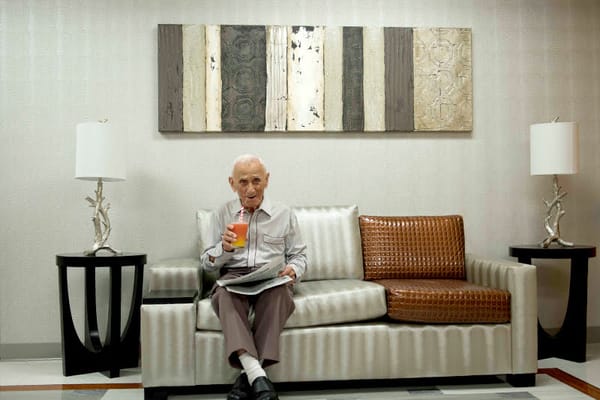 Elderly man sitting in a common area with a drink.