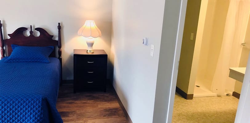 A bright private resident room with a bed and nightstand