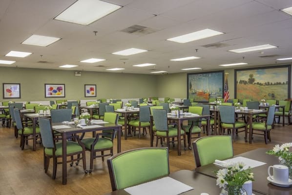 Bright dining room with green chairs and tables set for meals