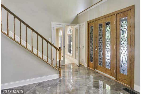Spacious entrance hallway with stairs and glass-paneled doors.