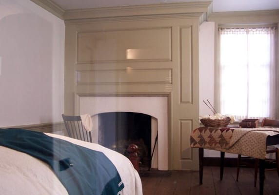 Interior view of a historical bedroom featuring a bed, fireplace, and table.