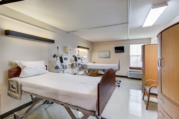 A view of a patient room with two hospital beds and medical equipment.