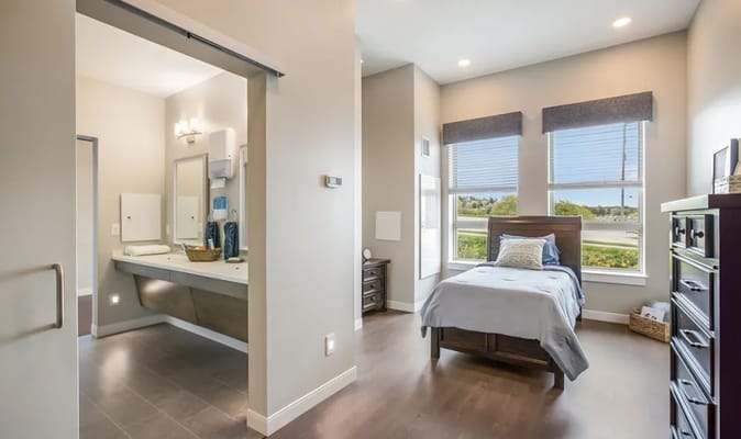 A well-lit bedroom with an attached bathroom in a senior living facility.